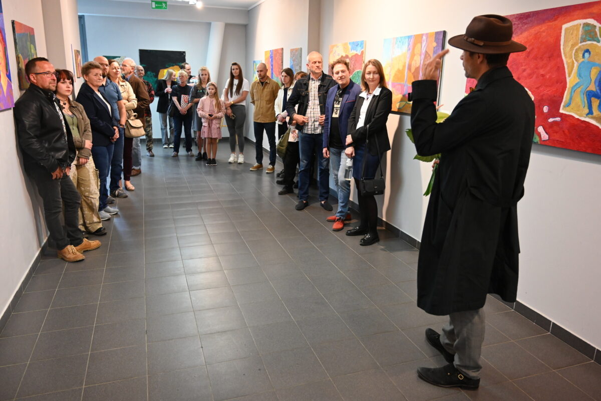 Artysta gestykulując opowiada publiczności o swoich pracach w galerii.